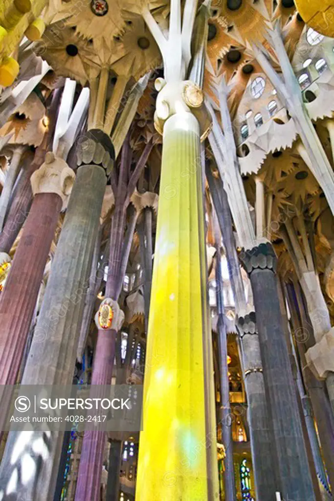 Barcelona, Catalonia, Spain, ornate stained glass window reflects color on columns and ceiling of the Interior of Sagrada Familia