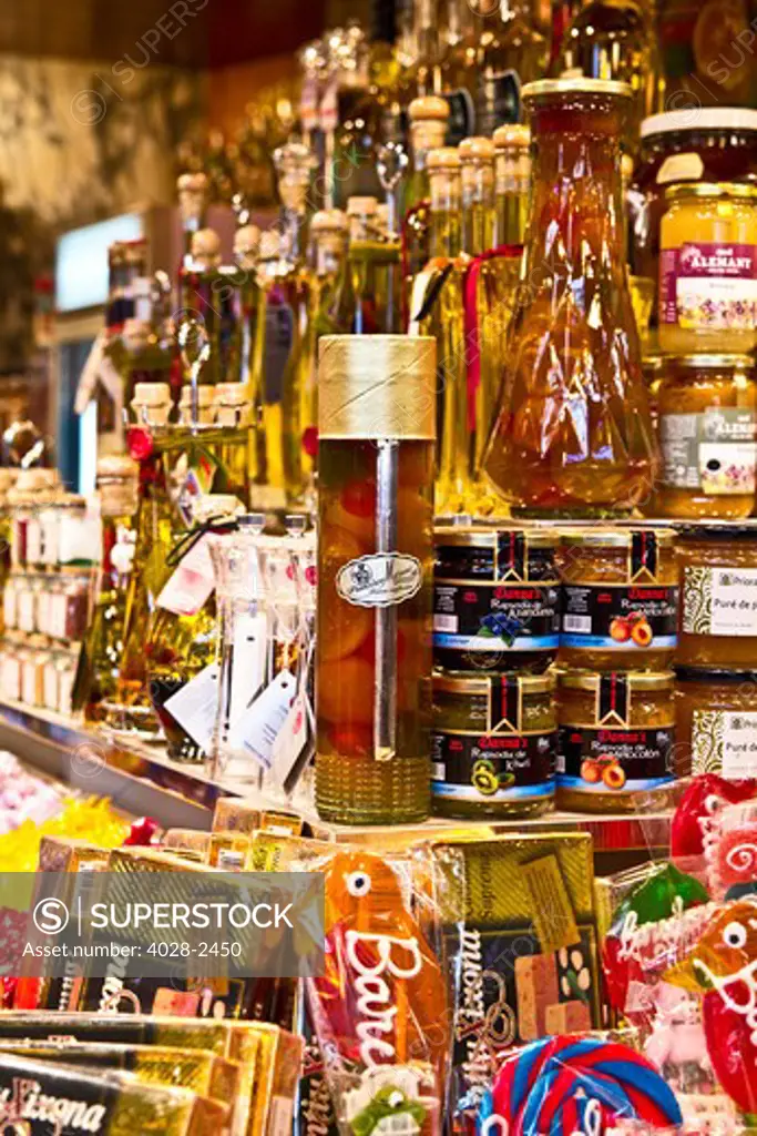 Barcelona, Catalonia, Spain, La Boqueria, La Rambla, vendors display and sell olive oils and candies in their market stall.