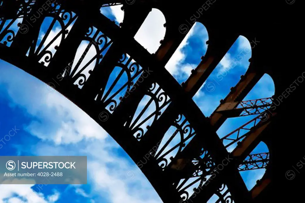 France, Paris, Detail of an Eiffel Tower (La Tour Eiffel) arch from underneath with a cloudy blue sky showing through