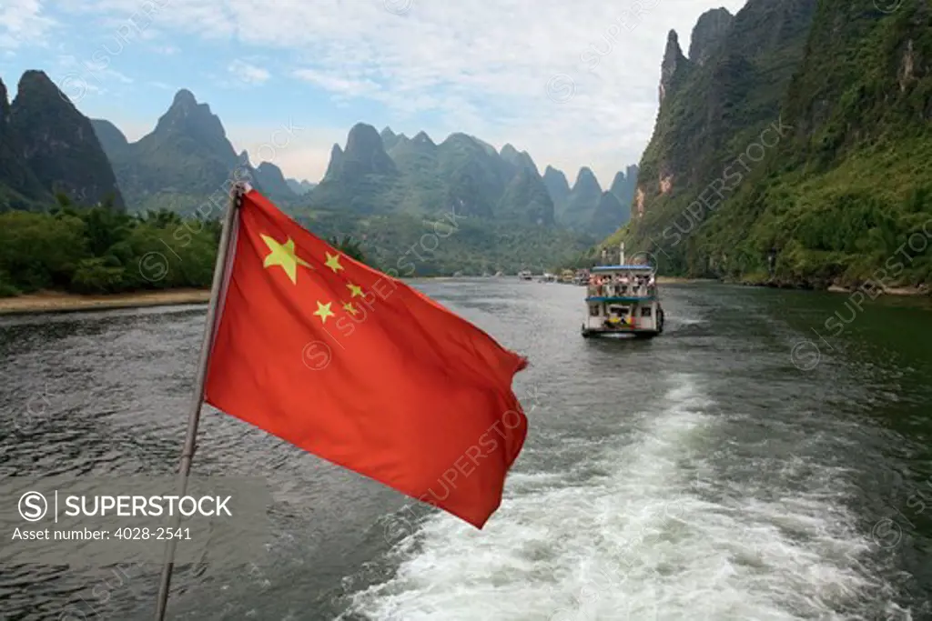 China, Guilin, Li River, River boats line the way along the River with it's dramatic mountains, Chinese Flag in the foreground.