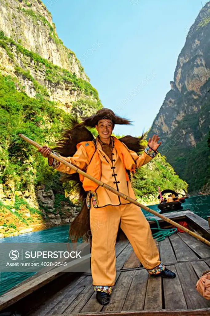 China, Guilin, Li River, A Cormorant Fisherman dressed in traditional clothes, waving as he paddles his way along the river, Sanpan Boats are in the background.