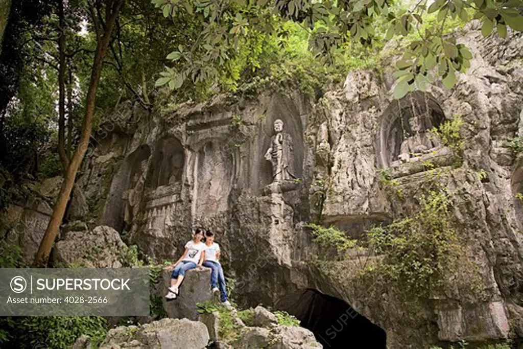 China, Hangzhou, Lingyin Buddhist Temple, Two girls pose in front of statues of Buddha carved into the mountain.