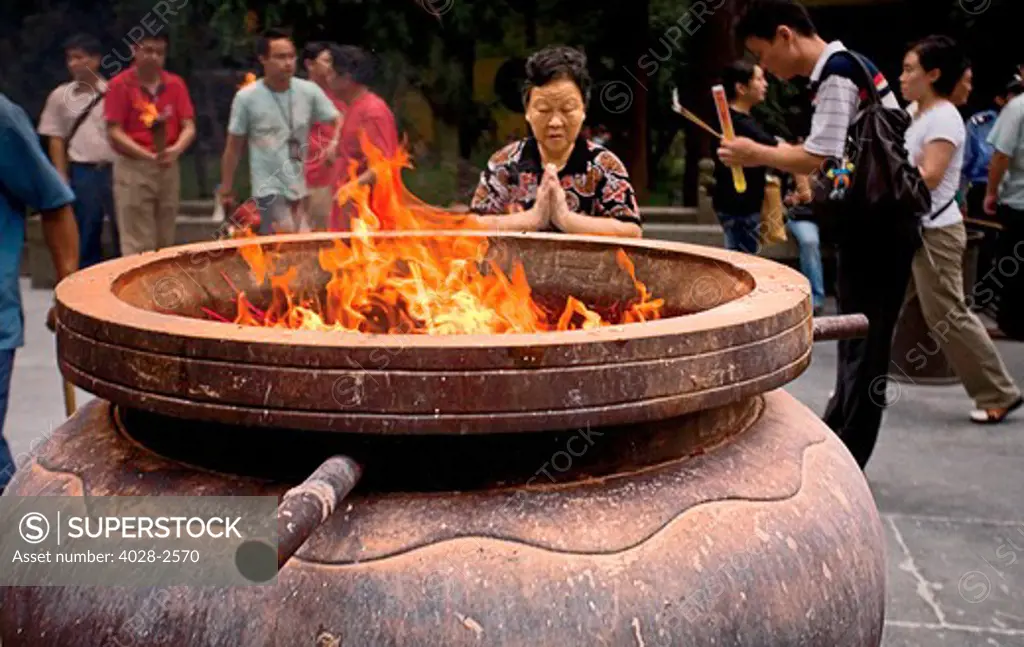 China, Hangzhou, Lingyin Buddhist Temple, An elderly Chinese woman prays in front of her burning offerings.