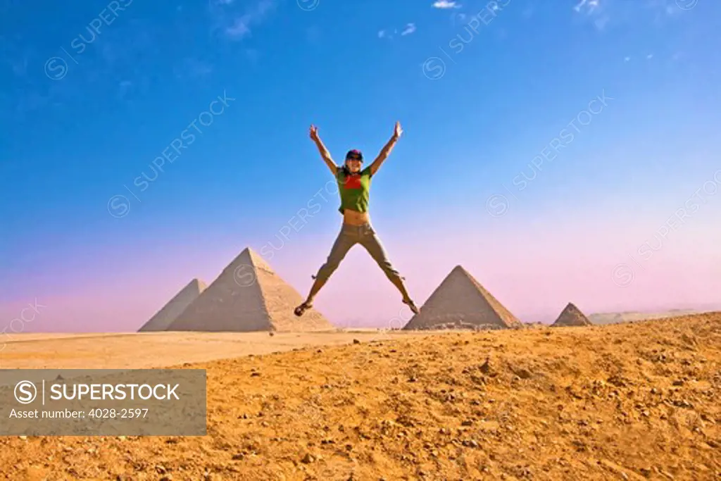 Egypt, Cairo, Giza, A woman jumps for joy in front of all three Great Pyramids forming another pyramid with the negative space of her legs.