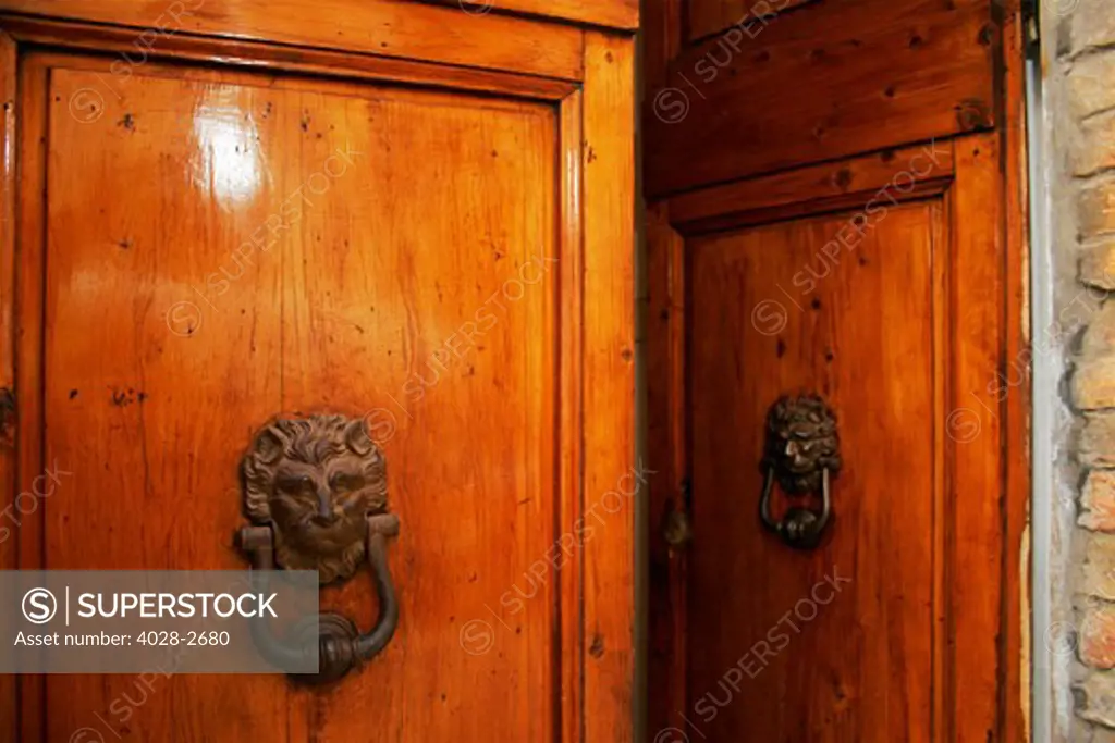 Florence, Italy, old iron door knockers in the shape of a male lion's head adorn richly laquered wooden doors
