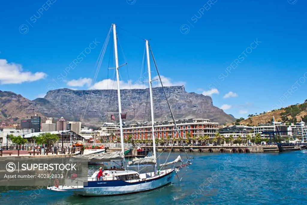Cape Town, South Africa, A sailboat sails through the Victoria and Albert waterfront with Table Mountain in the background