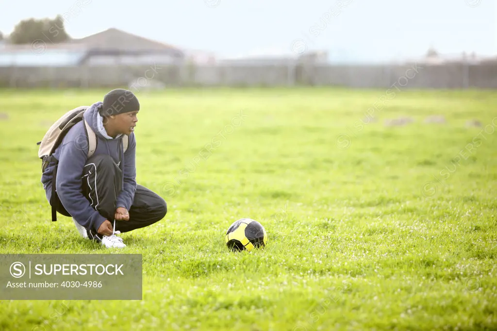 Boy tying shoelace next to soccer ball, Cape Town, South Africa