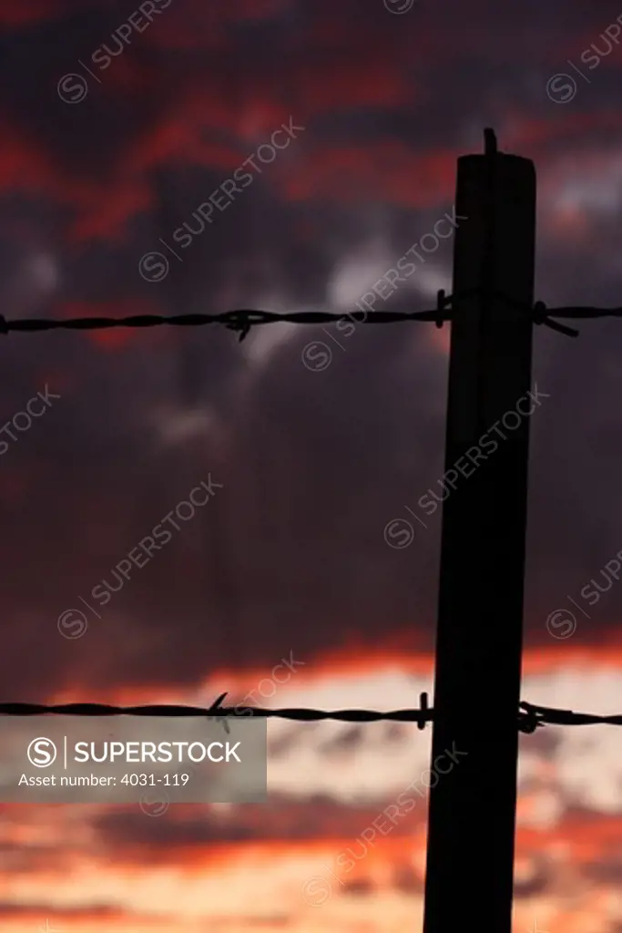 Fence post and barb wire silhouetted against a dramatic sunset sky. Stanislaus county, California, USA