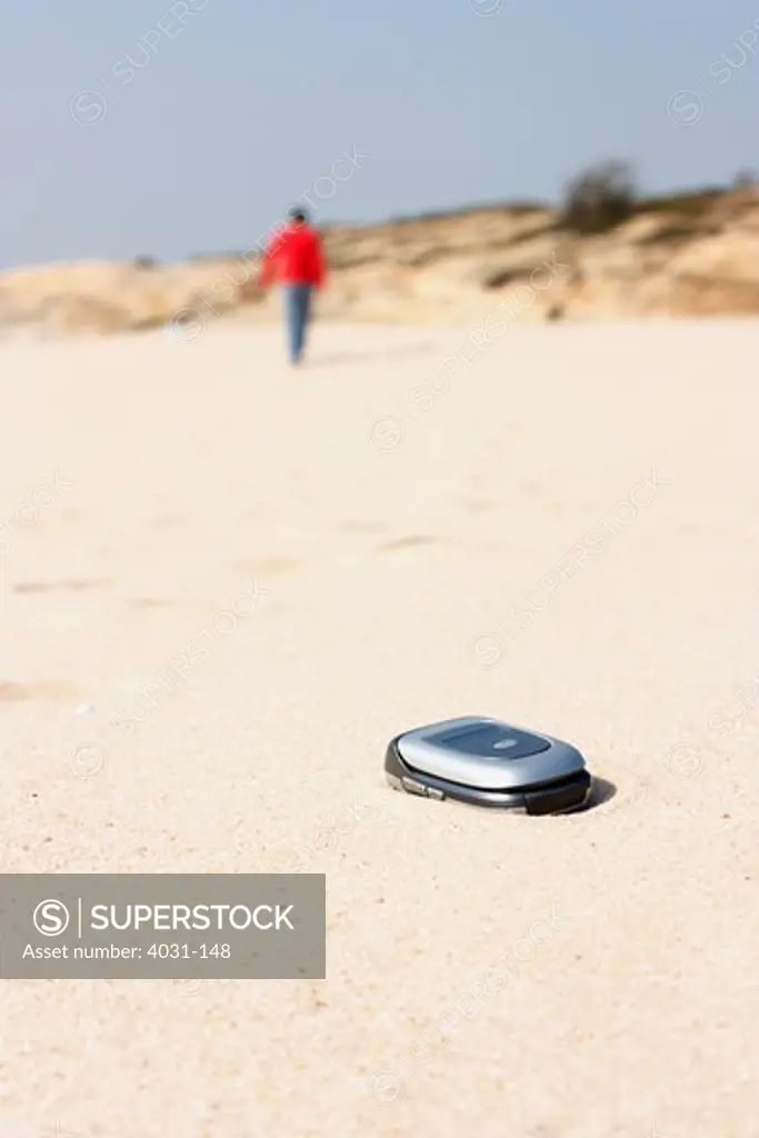 Mobile phone in the sand with a person walking away, Kinmen County, Taiwan