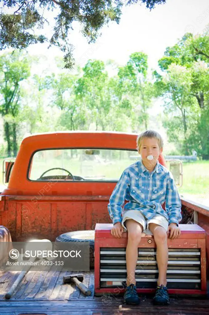 Boy sitting on a pick-up truck and blowing bubble gum, Bozeman, Gallatin County, Montana, USA