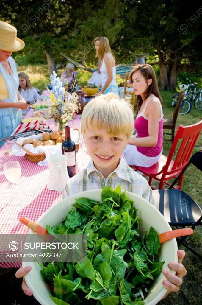 Boy holding a big bowl of salad with his family in the background, Bozeman, Gallatin County, Montana, USA
