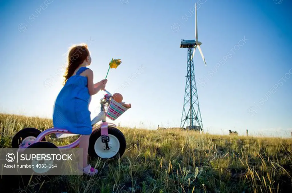 Girl holding a pinwheel and riding a tricycle near a wind turbine, Bozeman, Gallatin County, Montana, USA