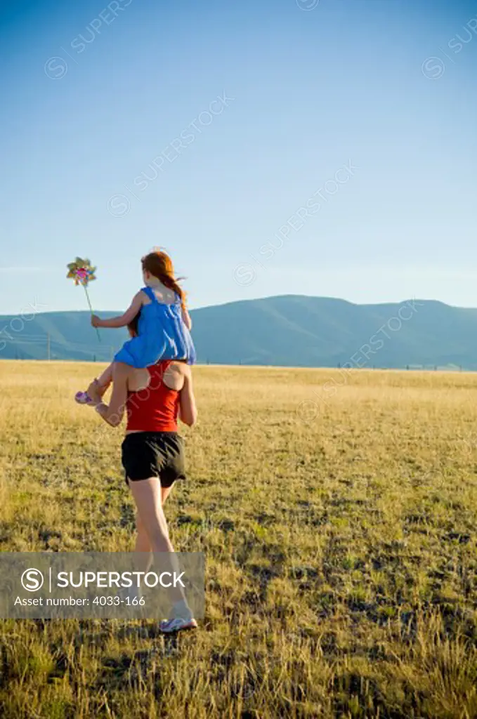 Young woman carrying her daughter on her shoulders in a field, Bozeman, Gallatin County, Montana, USA
