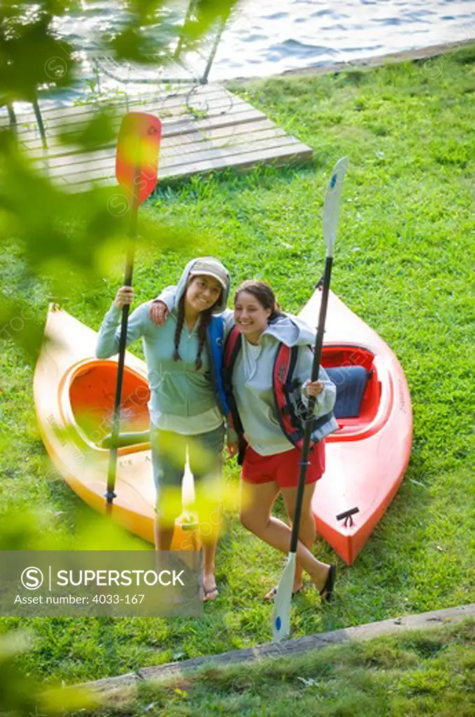 Two female friends standing beside kayaks, Ithaca, New York State, USA