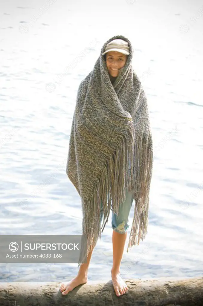Young woman wrapped in a shawl standing at the lakeside, Ithaca, New York State, USA