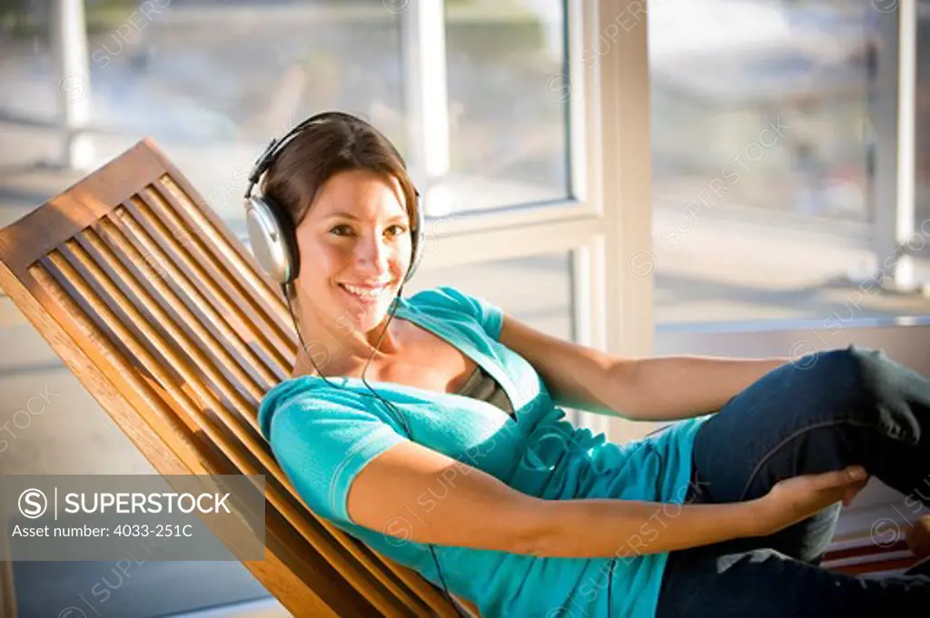Young woman resting on a lounge chair and listening to headphones, San Diego, California, USA