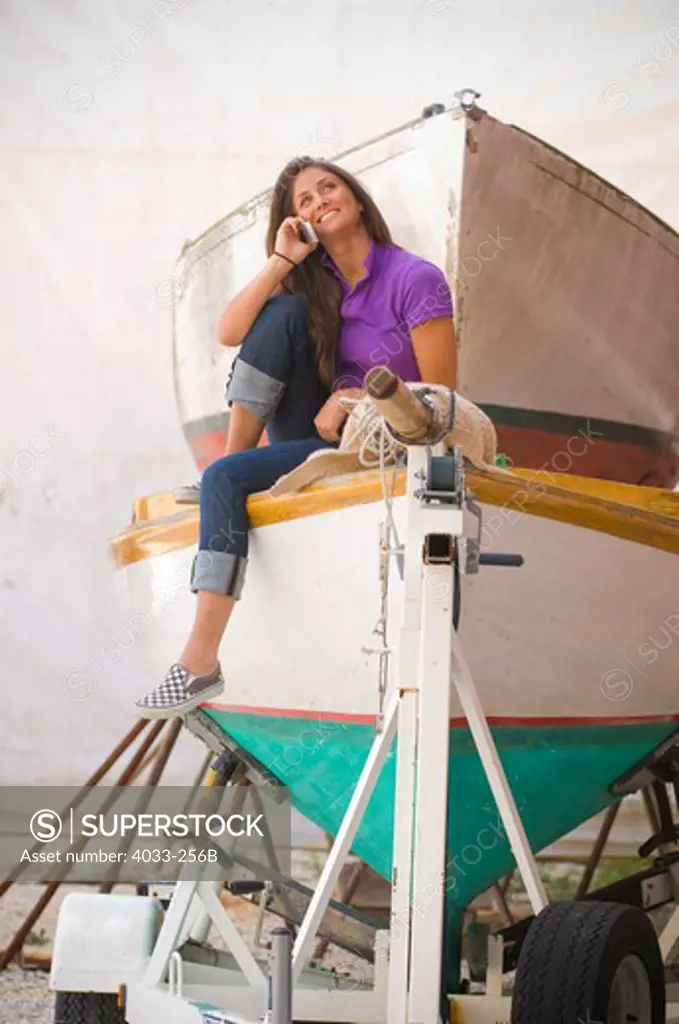 Young woman sitting on a sailboat talking on a mobile phone, Newport, Rhode Island, USA