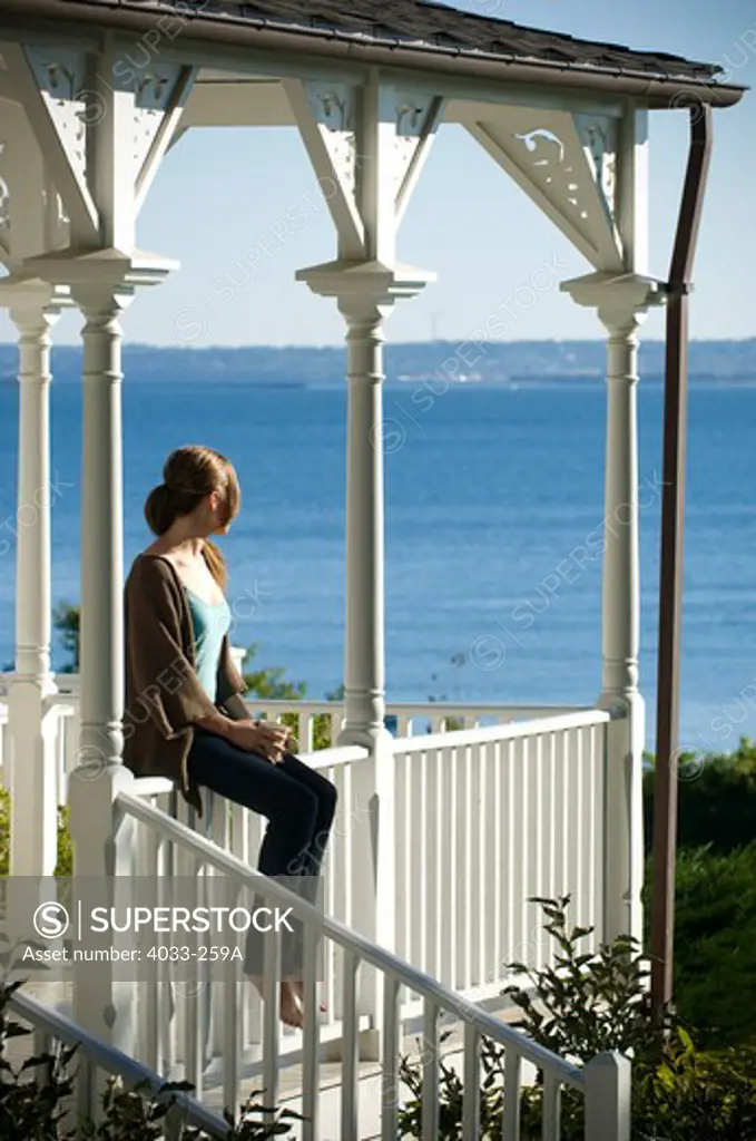 Young woman sitting on a porch railing, Jamestown, Rhode Island, USA