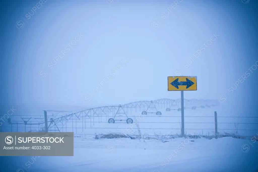 Double arrow sign in a snow covered field, Bozeman, Montana, USA