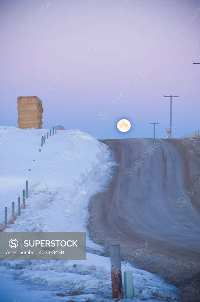 Rural road in winter with moonrise in the sky, Bozeman, Montana, USA