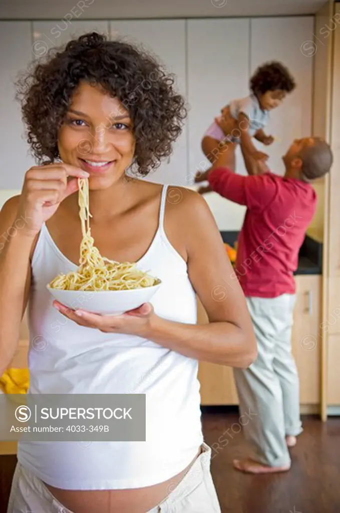 Pregnant woman eating pasta with her family in the background, San Diego, California, USA