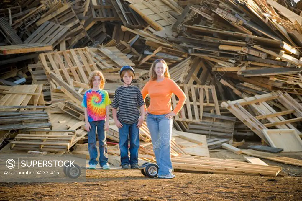 Young woman standing with her children in front of a heap of recyclable wooden products
