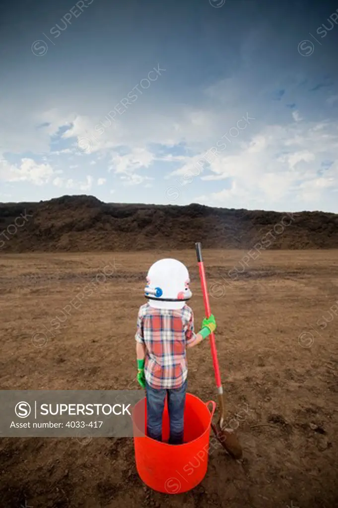 Boy wearing a space helmet and standing in a bucket at a landfill
