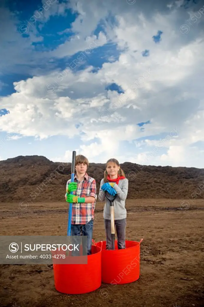 Boy and a girl standing in buckets with a mountain of compost in the background