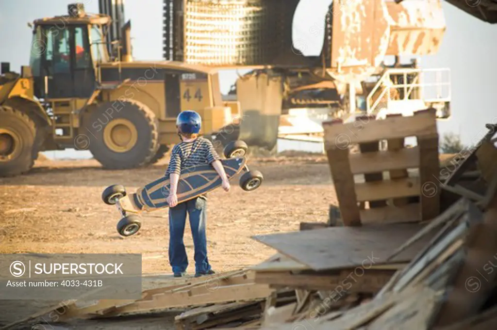 Boy with a skateboard watching heavy machinery at a landfill