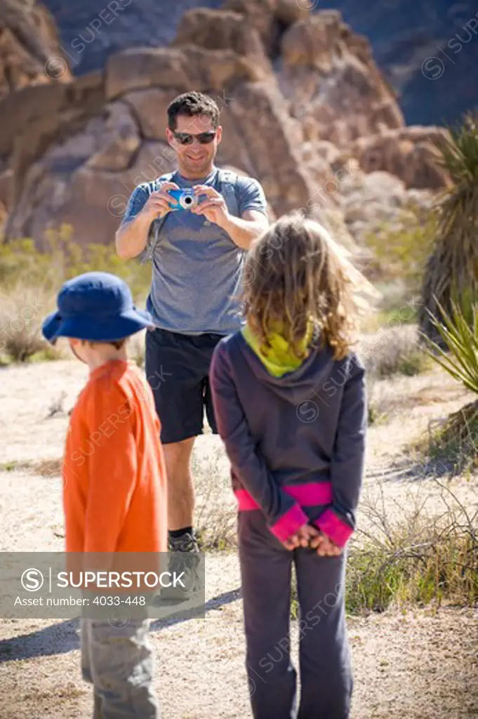 Mid adult man taking a picture of his children, Joshua Tree National Monument, California, USA