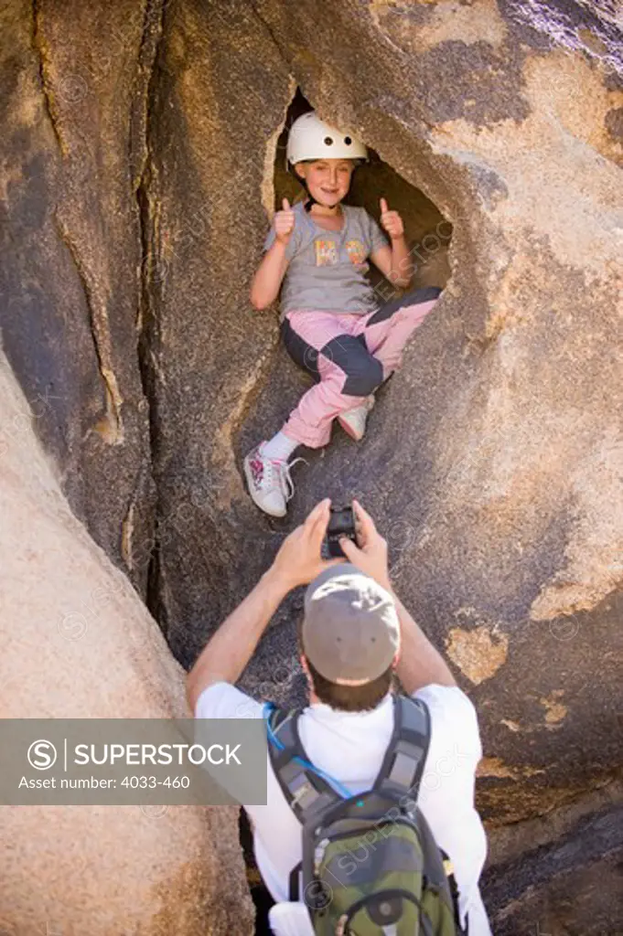 Girl sitting in a cave being filmed by her father, Joshua Tree National Monument, California, USA