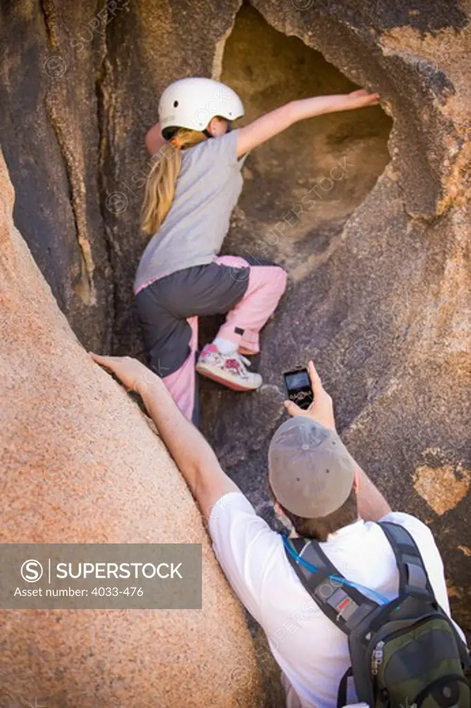 Girl rock climbing being filmed by her father, Joshua Tree National Monument, California, USA