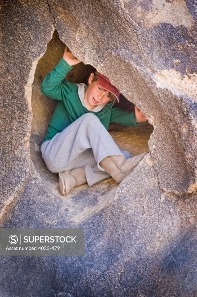 Boy sitting in a small cave, Joshua Tree National Monument, California, USA