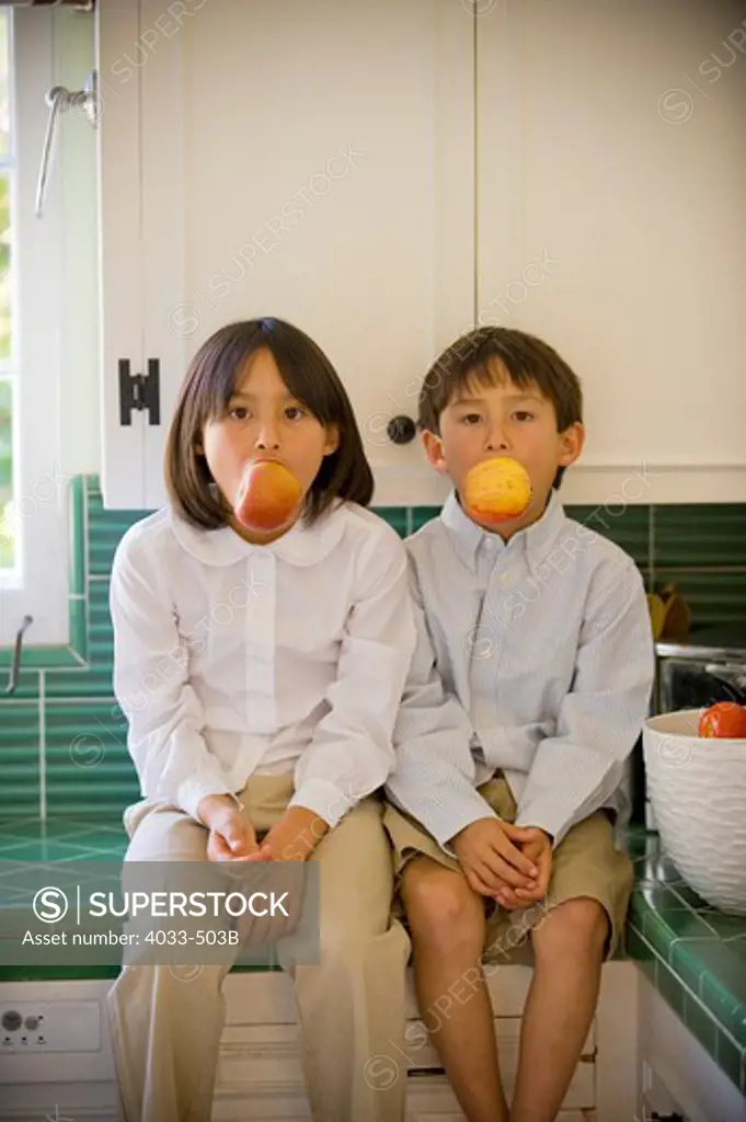 Boy and his sister sitting on a kitchen counter and eating apples