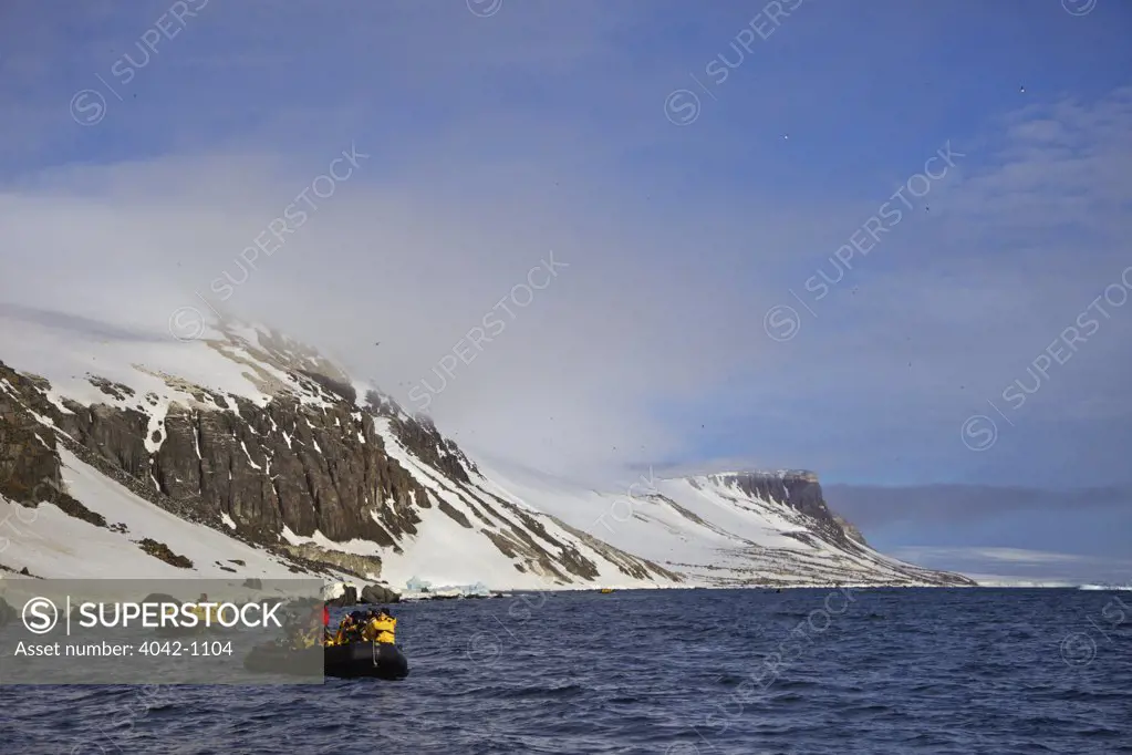 Tourists in zodiac inflatable near Alkefjellet cliffs, Spitsbergen, Svalbard Islands, Norway
