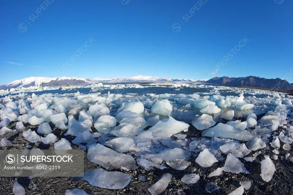 Iceland, Icebergs on glacial lake at Jokulsarlon with snow on massive icecap of Vatnajokull behind