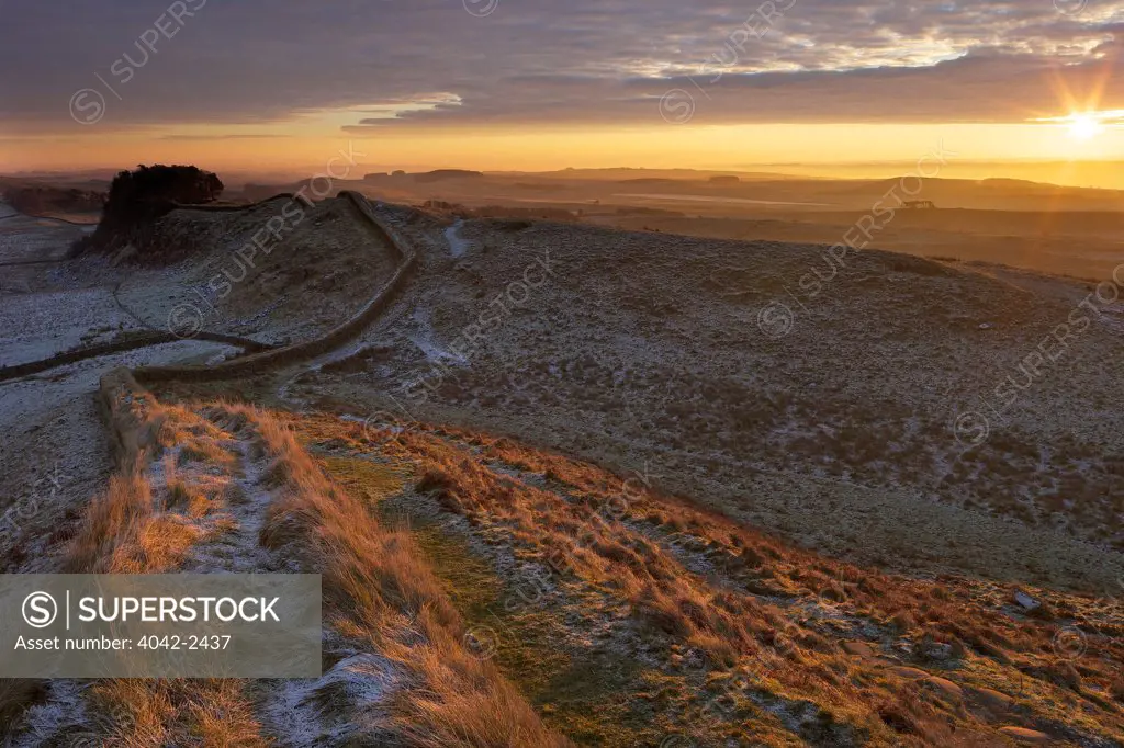 Sunrise over Hadrian's Wall National Trail in winter with Housesteads Fort from Cuddy's Crags in background, Northumberland, England