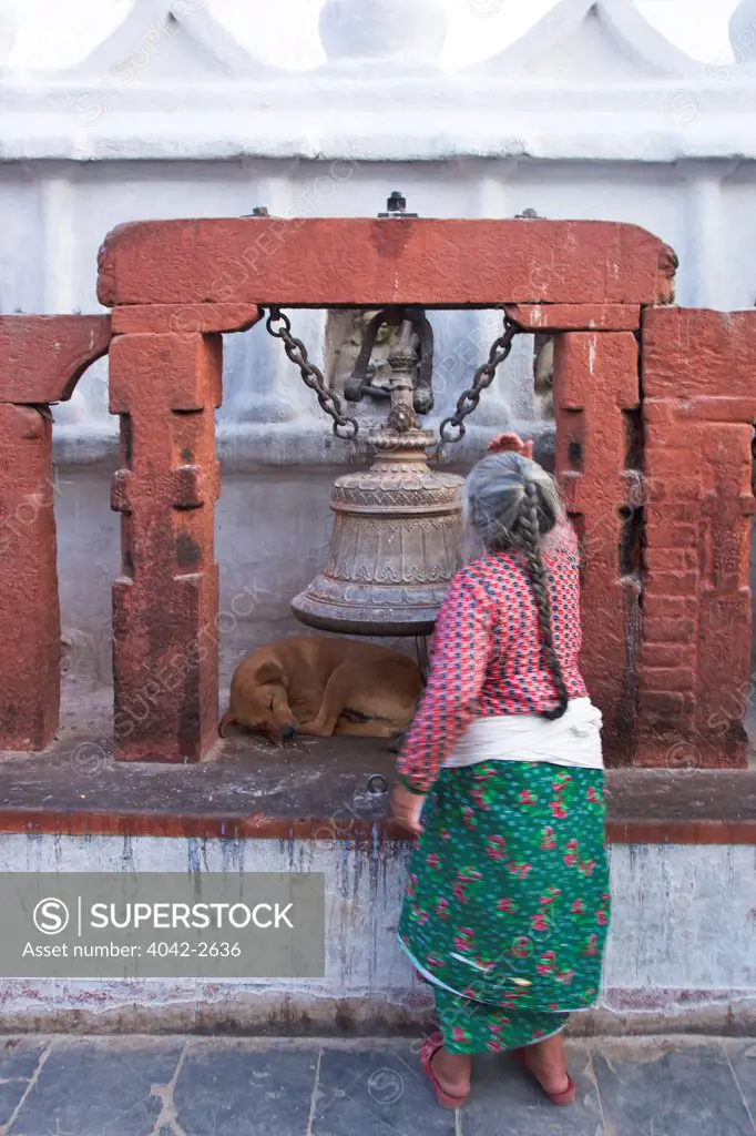 Old lady in front of bell and sleeping dog at Boudhanath Stupa, Kathmandu, Nepal