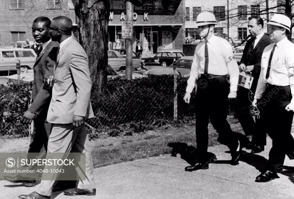 A Ku Klux Klan 'Security Patrol' walk behind Jeremiah X (left in light suit), leader of Atlanta's Black Muslim sect. Jeremiah X and an aide, were turned away when they attempted to tour downtown Hurt Park where Klan was having rally. March 22, 1964.
