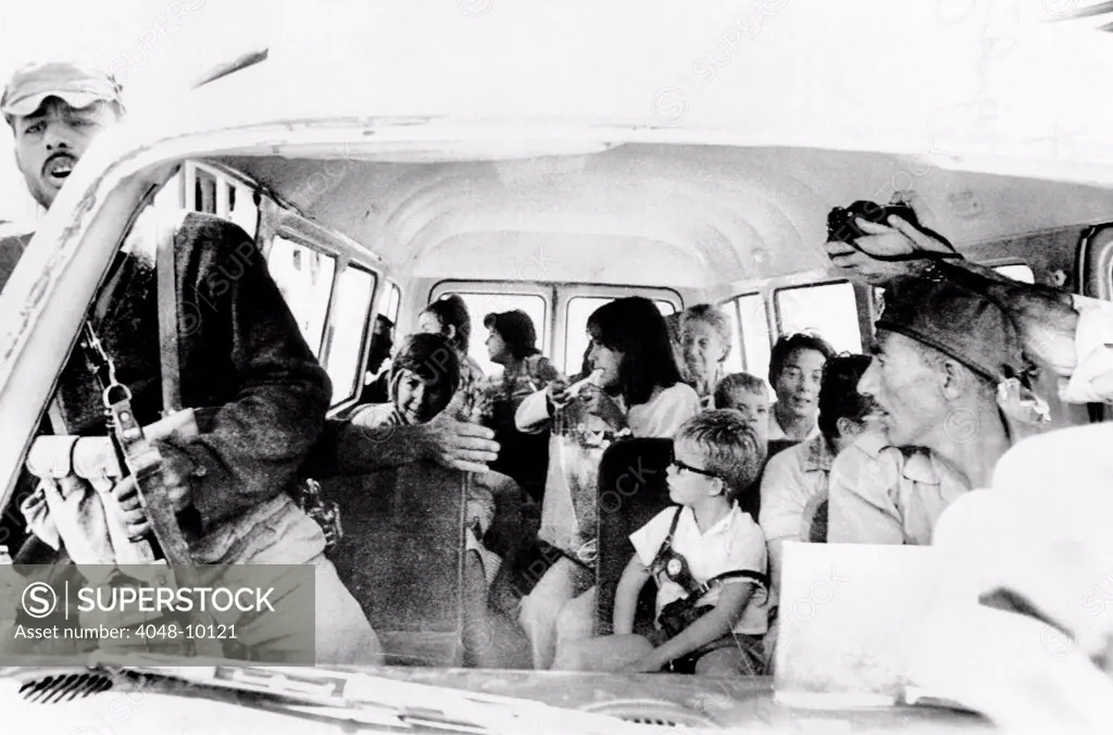 Women and children hostages about to be freed by the airline hijackers. They are arriving at the Intercontinental Hotel in Amman, Jordan. The hijacker with an automatic gun attempts to clear the road of newsmen as a photographer sticks his camera into the van. Sept. 12, 1970.