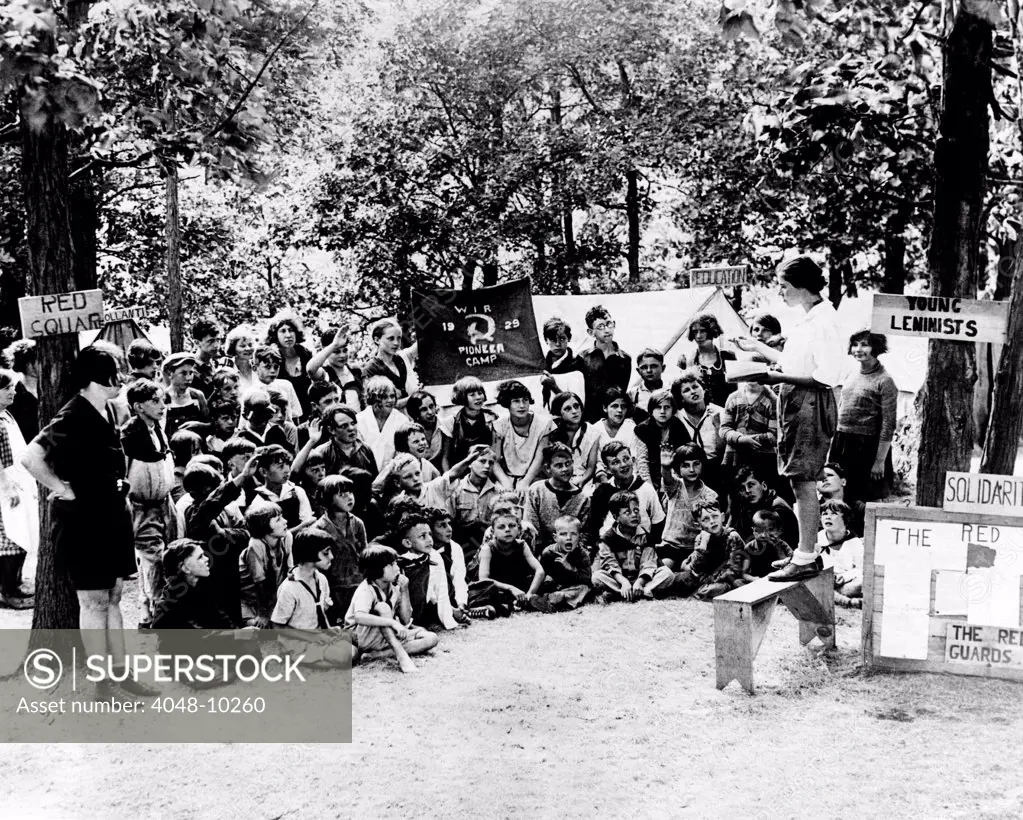 Chicago and Milwaukee youngsters are at a Communist summer camp. At Paddock Lake, Near Kenosha, Wisconsin, where Communist indoctrination joined hikes, swimming, sports as daily activities. Miss Eve Stolar, educational director of the camp, lectures on class struggle to the young campers. 1930s.