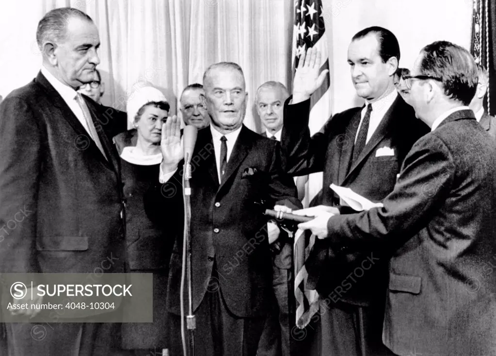 Vice Admiral W. F. Raborn is sworn in as CIA Director, and Richard Helms as Deputy Director. At the White House ceremony, L-R: President Lyndon Johnson, Adm. Raborn, Richard Helms, and Carson Howell. In background are Mrs. Helms, J. Edgar Hoover, and Paul Nitze. April 28, 1965.