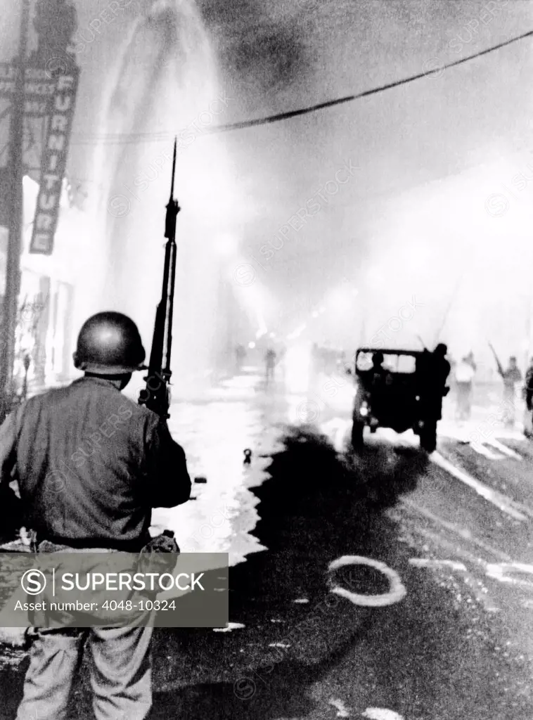 National Guard in Watts during the 1965 race riot. Debris litters the streets and a geyser from broken fire hydrant sprays at left. August 14, 1965.