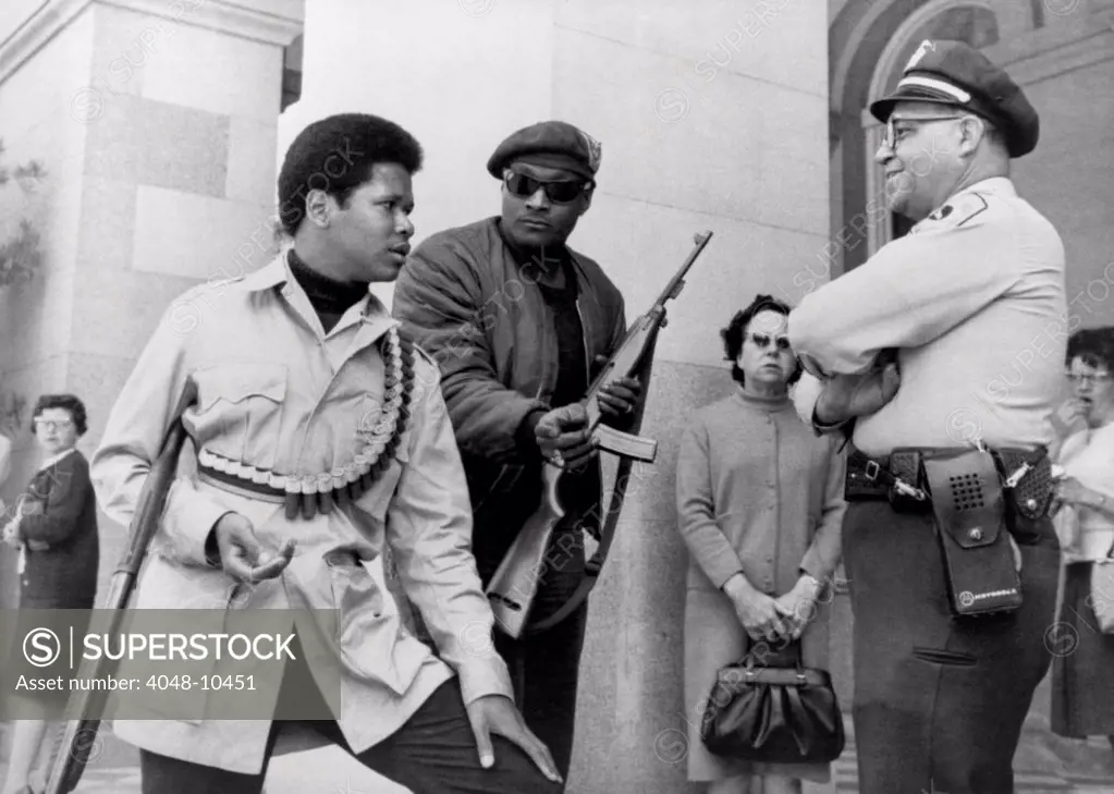 Two armed Black Panthers, carrying a shotgun, and a semi-automatic rifle, talking to officer Lt. Ernest Holloway at the State Capitol, Sacramento, California. The Panthers were protesting the state's selective ban on weapons. May 1967.