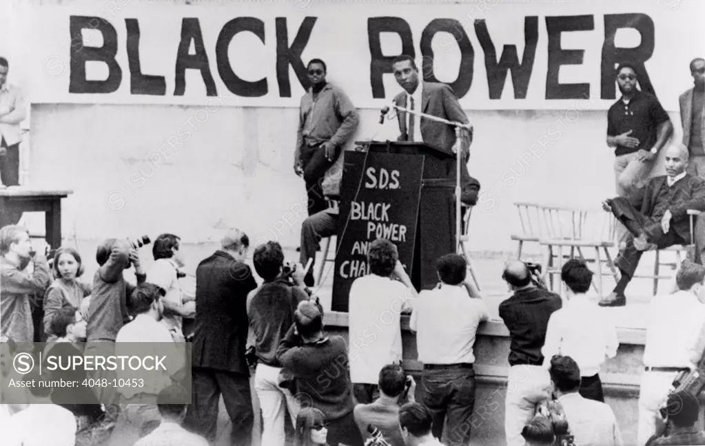 Stokely Carmichael speaking at the University of California at Berkeley. A large 'Black Power' sign and SDS initials for the leftist 'Students for a Democratic Society' are on the podium. Ca. 1965-67.