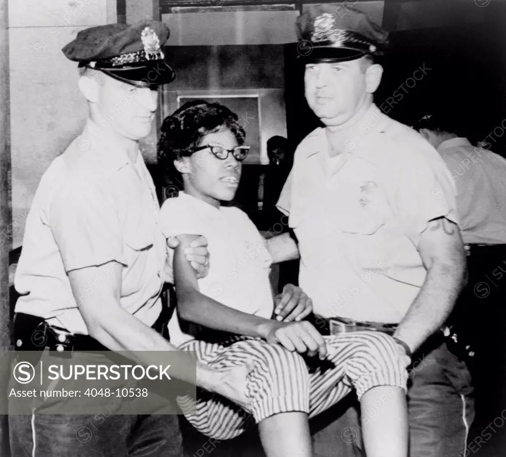 Two policemen carry a young African-American woman arrested during a sit-in at the First National Bank in St. Louis, Ill. Aug. 12, 1963.