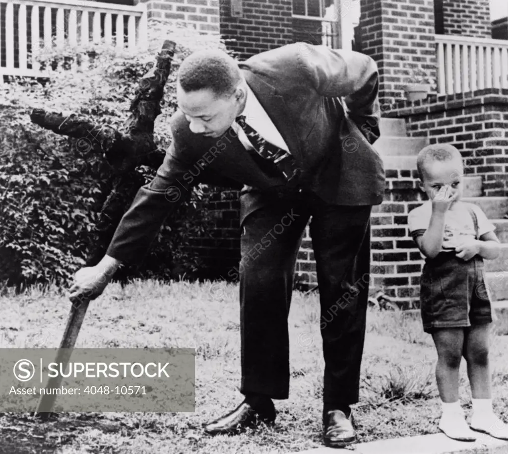 Martin Luther King, removes a KKK cross burned on lawn of his home, as his son Martin stands next to him, Atlanta, Georgia. April 27, 1960.
