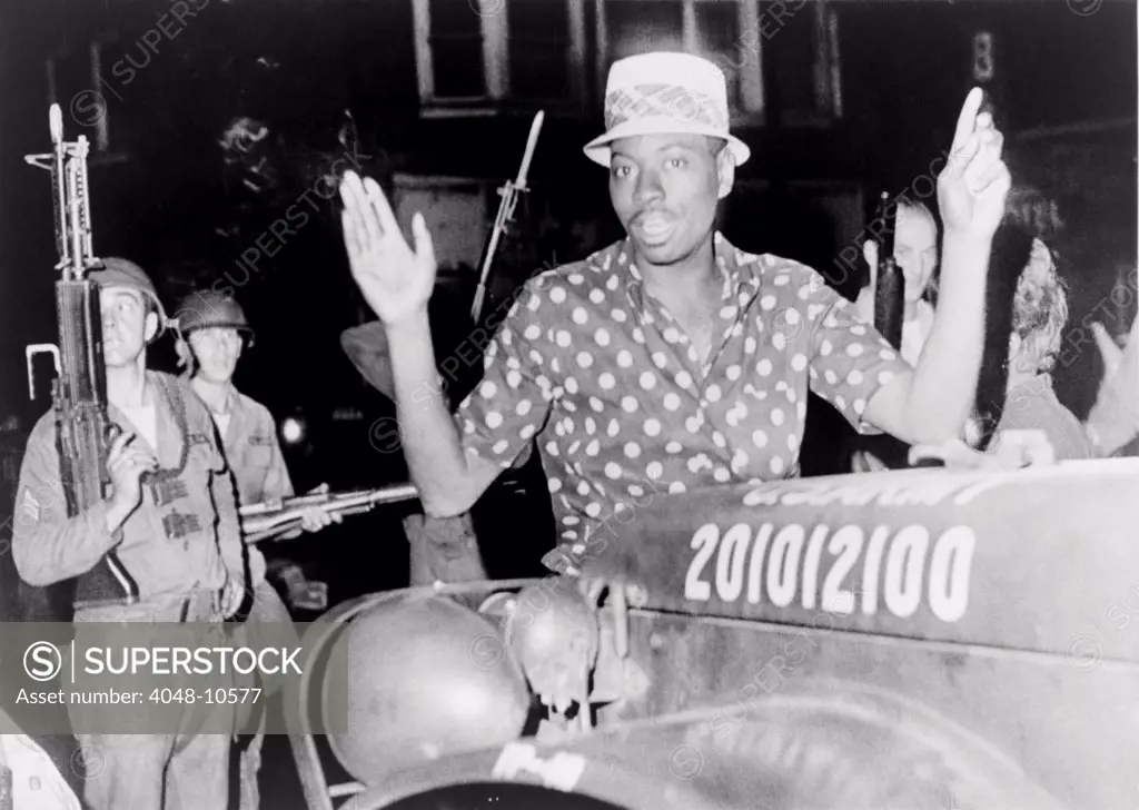 African American man with arms raised in the riot-torn Hough Avenue section of Cleveland, Ohio. The suspect was found with 13 bottles and the makings for 'Molotov cocktails' in his car. July 24, 1966.