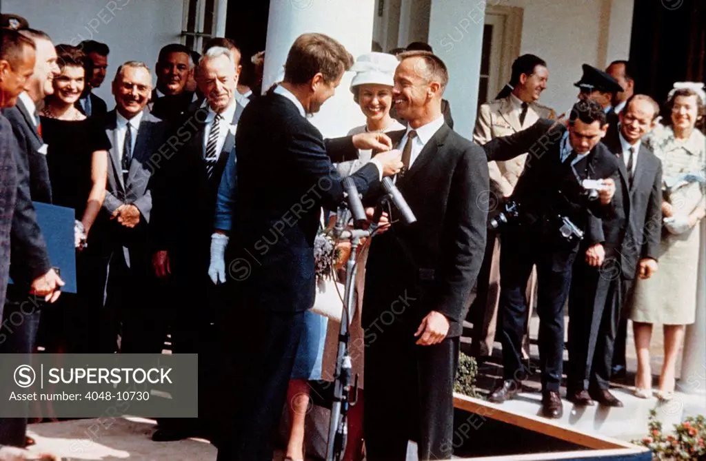 President Kennedy pins NASA's Distinguished Service Medal on the jacket of astronaut Alan Shepard in a Rose Garden ceremony. First Lady Jacqueline Kennedy and Mrs. Shepard are among the onlookers. May 8, 1961.