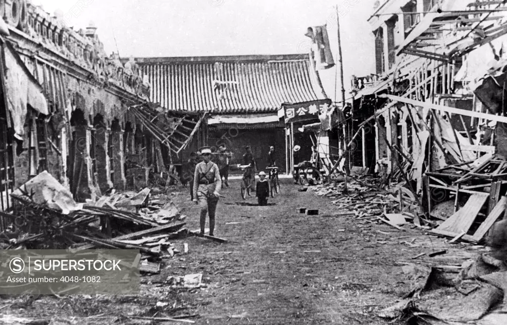 STREET SCENE IN TAIYUAN  Splintered ruins line this street in Taiyuan, principal city in North China, after Japanese bombing. A child stands in a shell-hole in the background. Note the bicycles behind him. 12/16/37.